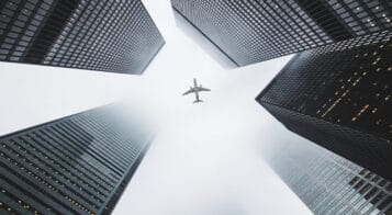airplane flying overhead framed by buildings